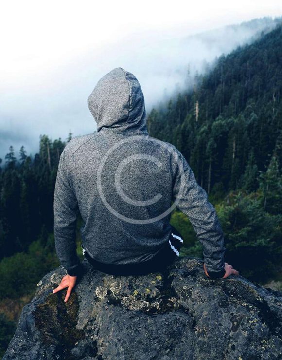 Hiker sitting on rock overlooking foggy forest valley